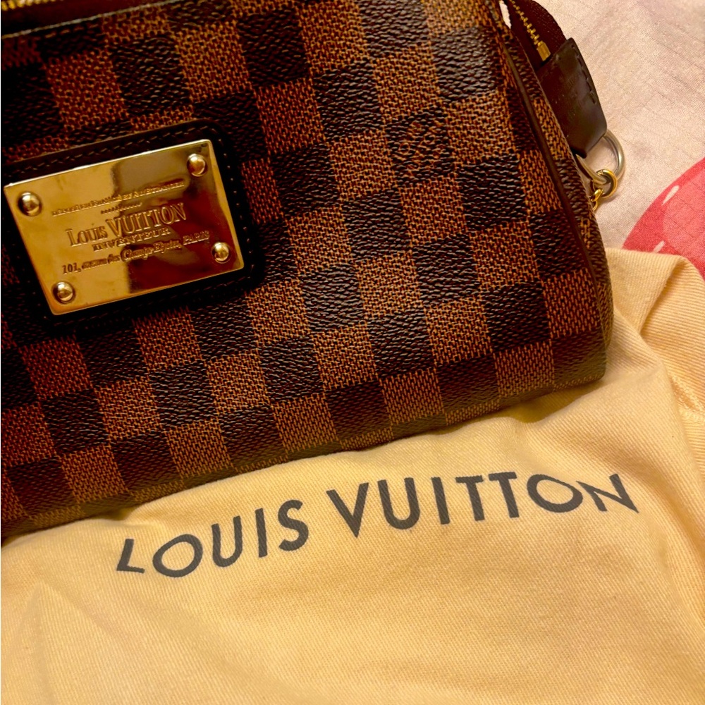 This is an authentic LOUIS VUITTON Damier Ebene Eva Clutch. This chic clutch